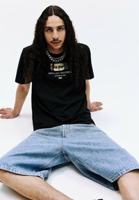 Sort grafisk t-shirt med et Mona Lisa-print og tekst, parret med lyseblå denim shorts med teksturerede mønstre og synlige syninger.