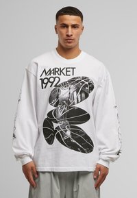 Hosszú ujjú fehér póló, fekete grafikával, rajta a "MARKET 1992" felirattal és tervezési elemekkel, beleértve absztrakt formákat és figurákat.