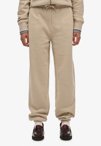 Pantaloni della tuta beige con vita regolabile, polsini affusolati e una texture morbida. Abbinati a mocassini neri e calze crema.