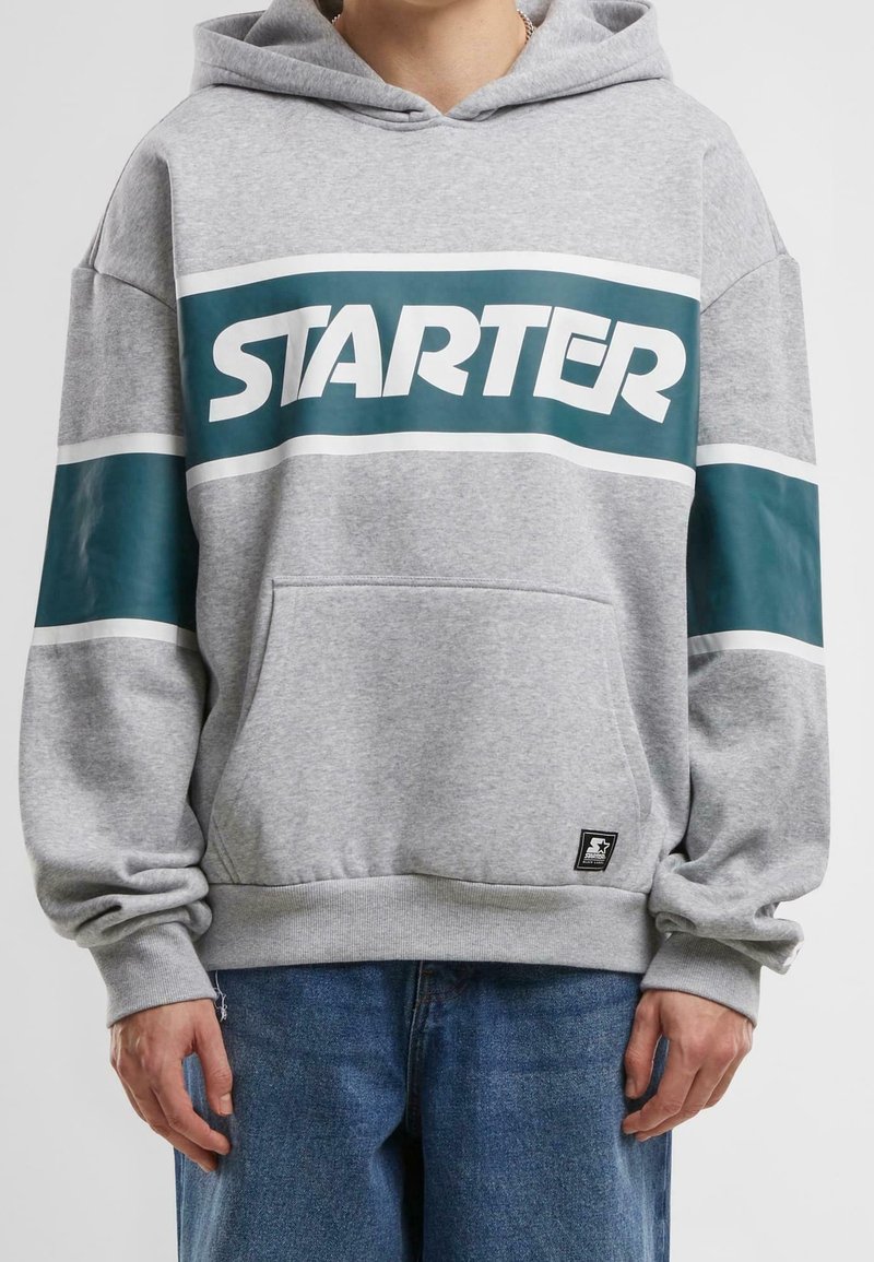 Sudadera gris con bolsillo frontal, que presenta un logo "STARTER" en color teal y rayas blancas en las mangas. Material de mezcla de algodón, ajuste relajado.