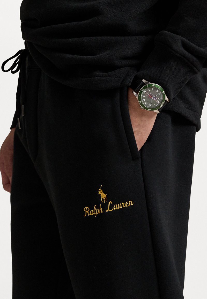 Sorte sweatpants med gyldent "Ralph Lauren" broderi og logo, der har en sidelomme og er parret med et ur med grønne accenter.