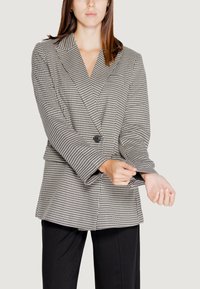Blazer a scacchi in bianco e nero con colletto a scollatura, chiusura con un solo bottone e maniche larghe, abbinato a pantaloni neri.