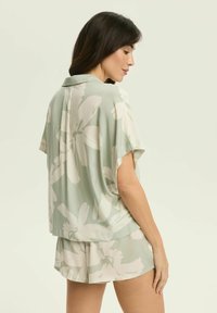 Zestaw odzieży domowej z krótkim rękawem w jasnym zielonym kolorze z dużym białym wzorem kwiatowym. Wykonany z gładkiego materiału, z ko łnierzykiem i luźnym krojem.