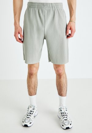 Grå ribbede shorts med elastik i taljen, der når til midt på låret, kombineret med hvide crew-sokker og sort-hvide sportssko.