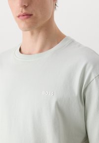 Mintgrønn bomulls T-skjorte med rund hals og korte ermer, med en hvit "BOSS" logo på brystet. Glatt tekstur.
