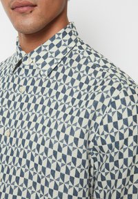 Hemd aus Baumwollstoff mit geometrischem Muster in Marineblau und Creme. Klassischer Kragen und dezente Textur.