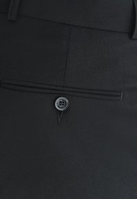 Czarne spodnie o teksturowanym wykończeniu, z tylną kieszenią i okrągłym czarnym guzikiem z detalem z nici.