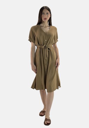 Vestido marrón con botones y mangas cortas enrolladas, con un cinturón de lazo en la cintura y una falda fluida. Llevado con sandalias marrones. Textura suave.
