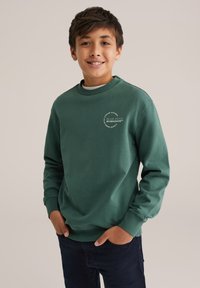 Hanorac din bumbac verde, cu guler rotund, mâneci lungi, manșete cu nervuri și un detaliu circular al logo-ului pe piept. Purtați-l cu blugi închiși la culoare.