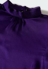 Lila Bluse mit hohem, gefaltetem Kragen, Knopfverschluss und glatter, satinähnlicher Textur. Hat geraffte Details am Halsausschnitt.