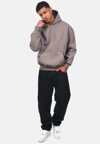Grauer übergroßer Hoodie mit Fronttasche, getragen mit lockeren schwarzen Hosen und weißen Sneakern, mit einem lässigen Schnitt und gerippten Bündchen.