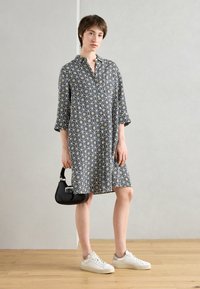 Abito bianco e nero con motivo floreale, colletto con bottoni, maniche a tre quarti, lunghezza al ginocchio, abbinato a una borsa nera e sneakers bianche.