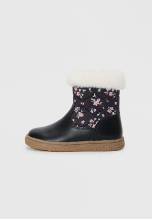 Bottine en cuir noir avec un tissu matelassé floral, un revers en fausse fourrure blanche et une semelle beige texturée. Présente un design à bout rond.