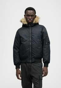 Μαύρο bomber jacket με ψεύτικη γούνα στην κουκούλα, κλείσιμο με φερμουάρ, ριμπ μανσέτες και τσέπη στο μανίκι. Λείος υλικό με επενδεδυμένο σχέδιο.