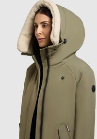 Olivengrønt isoleret jakke med en stor krämfarvet faux fur-beklædt hætte, frontlynlås, brystlogo og lynlåslommer i siderne.