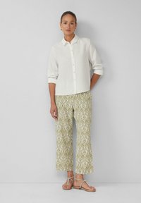 Weißes Leinen-Hemd mit Knopfleiste, hochgekrempelte Ärmel, kombiniert mit weiten grünen Hose mit einem Blattmuster. Sandalen runden das Outfit ab.
