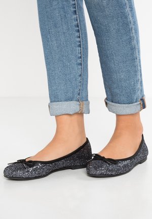 Czarne i srebrne baleriny z cekinami, z okrągłym noskiem i kokardką, zestawione z podwiniętymi jasnymi niebieskimi jeansami.