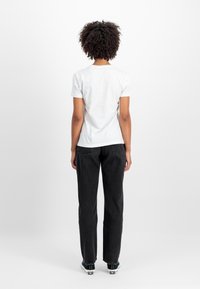 Bijela kratka majica s kratkim rukavima u kombinaciji s crnim trapericama visokog struka i crnim tenisicama. Glatka tkanina, opušteni kroj, jednostavan dizajn.