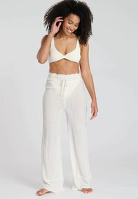 Bralette di crema chiaro con texture intrecciata, abbinato a pantaloni fluidi a vita alta con righe verticali e una cintura elastica.