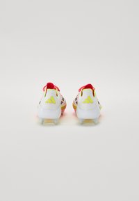 White soccer cleats with neon yellow accents and red laces. Features a textured upper and a translucent outsole with conical studs.