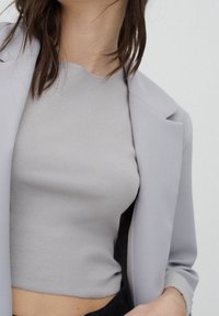 Crop top gris côtelé associé à un blazer gris clair, avec un tissu lisse, des épaules structurées et une coupe cintrée.