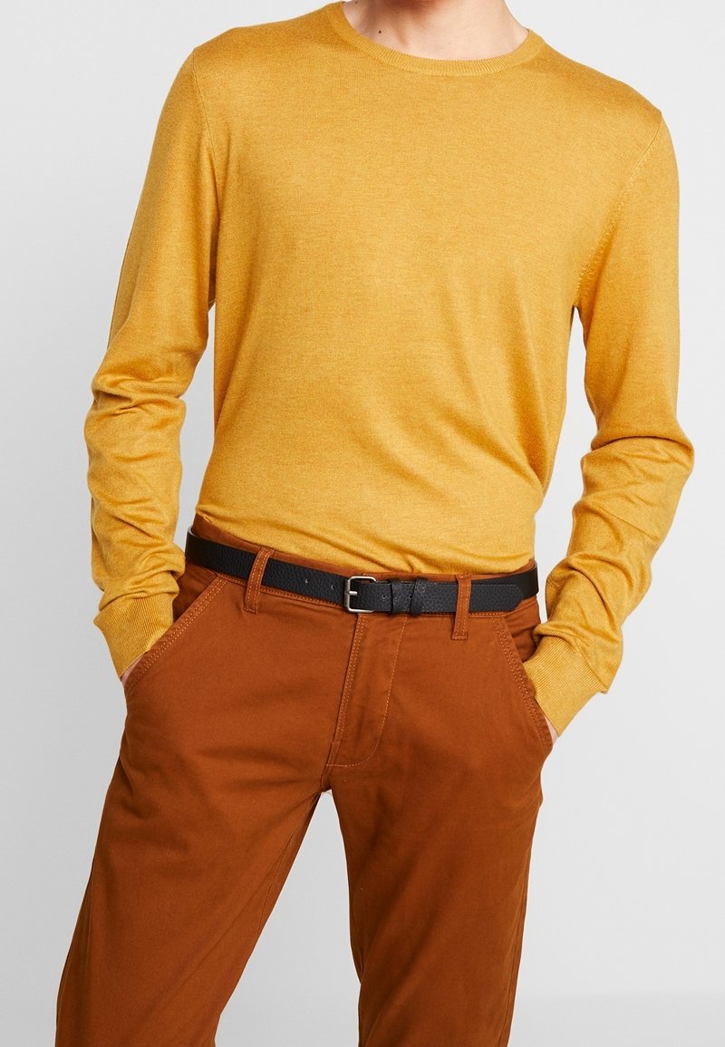 Senapsgul långärmad tröja med rund hals, tillsammans med bruna byxor och ett svart bälte med spänne. Slät, lätt material.