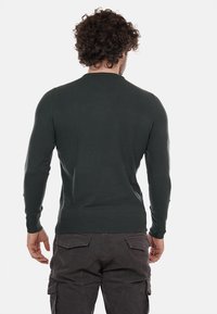 S sweater de punto verde oscuro con un escote redondo y mangas largas, que presenta un diseño ajustado y puños y dobladillo acanalados.