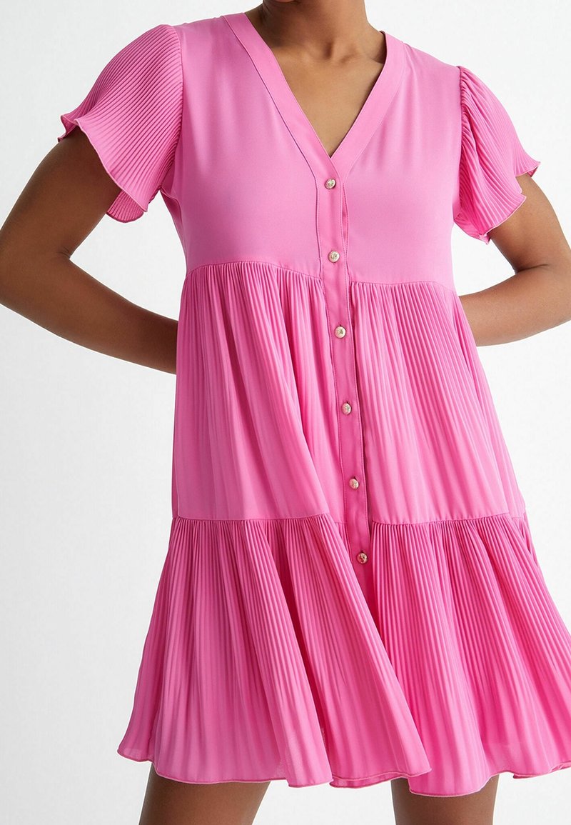 Vestido rosa plisado con escote en V, mangas cortas abullonadas y cierre de botones. Presenta una tela texturizada y una silueta en capas y fluida.