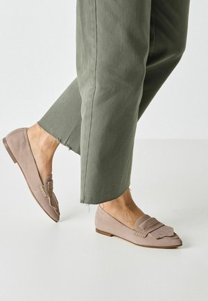 Light pink suede loafers with a decorative fringe and layered strap. Low-profile design and flat sole, paired with cropped olive green trousers.