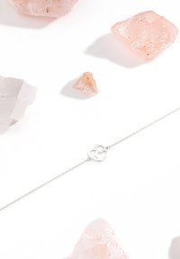 Silverarmband med ett dubbelhjärtcharm, omgiven av oregelbundna rosa kristallbitar mot en vit bakgrund.