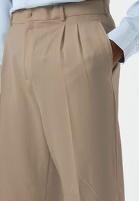 Beige trousers with a relaxed fit and pleated front, made from smooth fabric; features belt loops and side pockets.