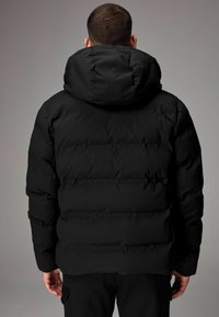 Sort puffjakke med hætte, der har et quiltet design og en glat overflade. Bagfra viser den en afslappet pasform og justerbare elementer.