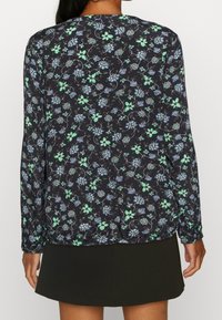 Blouse florale sombre à manches longues, présentant un imprimé bleu et vert sur fond noir. Tissu doux avec une coupe ample, encolure ronde.