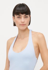 Svijetloplava halter topica s dubokim V-izrezom, izrađena od mekog, rastezljivog materijala. Ima elegantan dizajn i minimalan hardware.