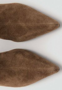 Zapatos de ante marrón con punta puntiaguda que presentan una textura suave con un brillo sutil, suela plana y detalle de costura central a lo largo del frente.