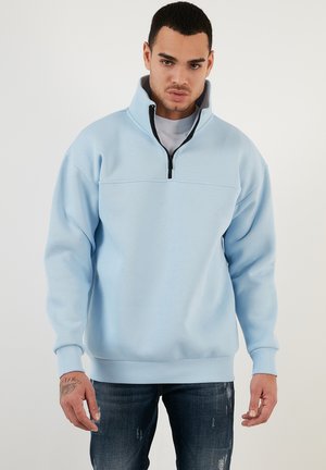 Felpa azzurra chiara con mezza zip, polsini a coste e una texture uniforme. Presenta un colletto alto e una cucitura orizzontale sul petto.