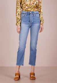 Jeans a vita alta di un leggero blu con taglio dritto, dotati di un design a quattro tasche e orlo pulito, abbinati a tacchi aperti color sabbia.