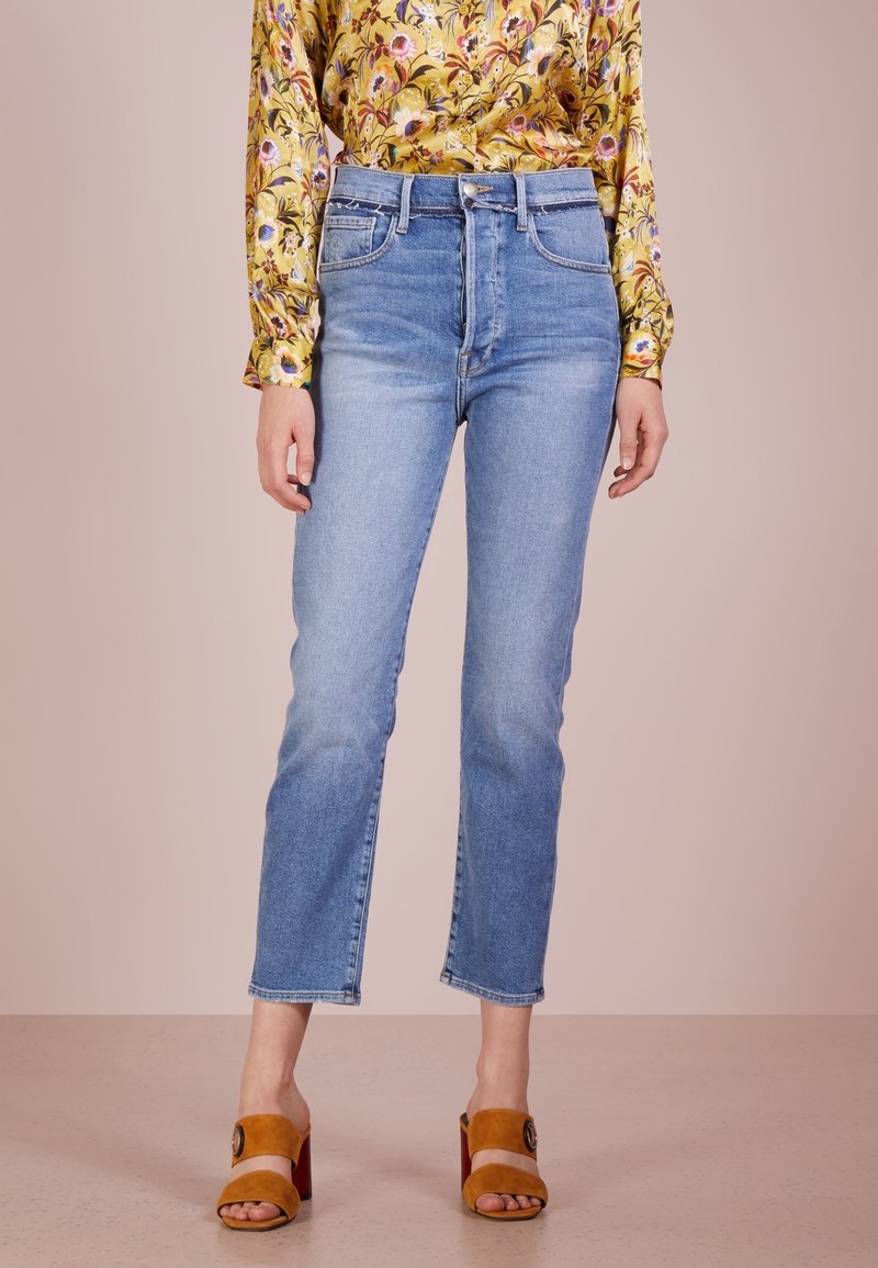 Jeans a vita alta di un leggero blu con taglio dritto, dotati di un design a quattro tasche e orlo pulito, abbinati a tacchi aperti color sabbia.