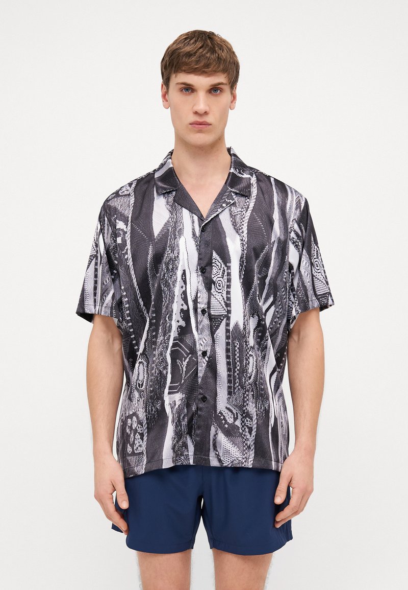 Short-sleeve shirt in black and white with abstract patterns. Lightweight fabric, collar design, and button front detail. Casual style.