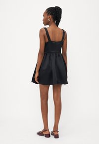 Melna satīna kleita ar regulējamām siksnām, pieguļošu bodi un platām svārku kārtām ar gludu tekstūru un diskrētu aizmugurējo rāvējslēdzēju.