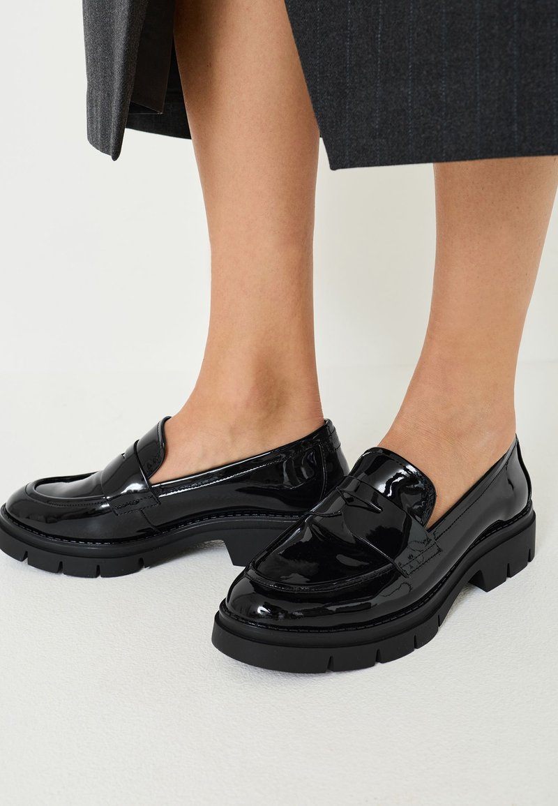 Svarta lackläder loafers med en tjock plattformssula och slät yta, med ett dekorativt band över framsidan.