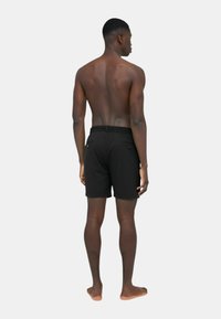 Pantaloni da bagno neri con vita aderente e cordino, dotati di tasche posteriori e in un tessuto leggero e liscio. Modello mostrato di spalle.