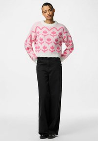 Maglione lavorato a maglia con motivi floreali rosa su sfondo bianco, maniche ampie e scollatura rotonda, abbinato a pantaloni neri a vita alta.