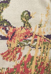 Tissu tricoté présentant un motif multicolore avec des teintes rouges, vertes, jaunes et violettes sur un fond crème, créant un design texturé.