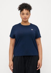 Marineblå bomulds T-shirt med korte ærmer og rund halsudskæring. Har et lille hvidt broderet logo på brystet. Løs pasform.