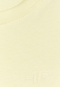Gros plan sur un tissu jaune pâle avec un col rond et un logo "4F" brodé en blanc en bas à droite.