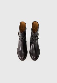 Par de botas de cuero marrón oscuro hasta el tobillo con cremalleras laterales y correas con hebilla, vistas desde arriba sobre un fondo blanco.
