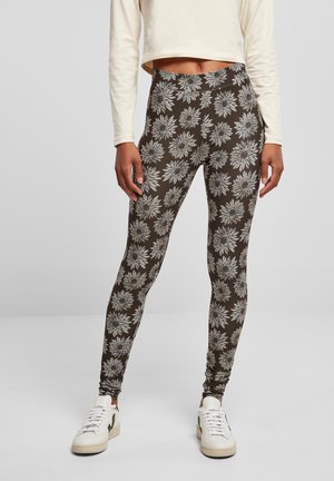 Leggings marron ornés d'un motif floral blanc. Confectionnés en matière extensible, ils ont une taille haute et sont associés à des baskets blanches.
