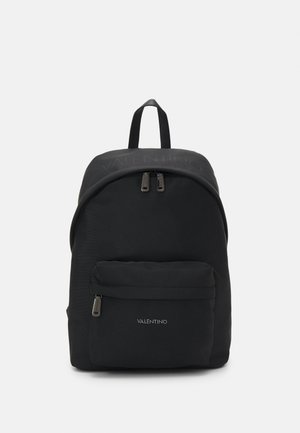 Mochila negra de nylon con parte superior redondeada, dos compartimentos con cremallera y bolsillo frontal. Presenta un sutil detalle del logotipo y una textura de tela resistente.