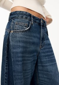 High-waisted dark blue denim jeans with a relaxed fit, featuring front pockets, belt loops, and subtle fading along the fabric.